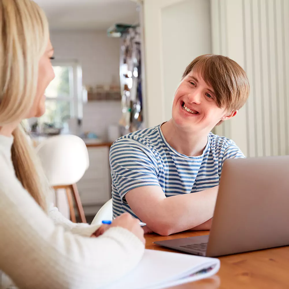 Disabled man smiling and sitting with his support worker with a laptop and papers on the table