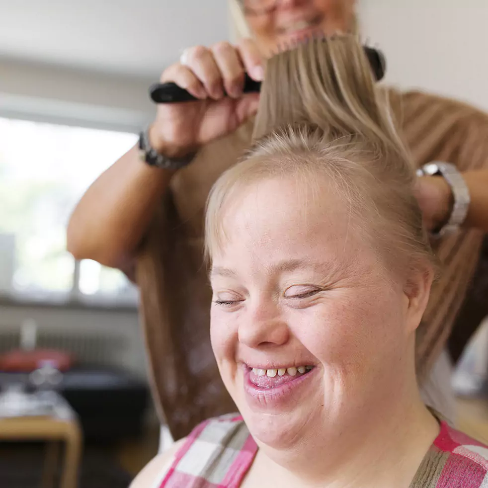Disabled woman smiling while sitting down and her support worker is brushing her hair
