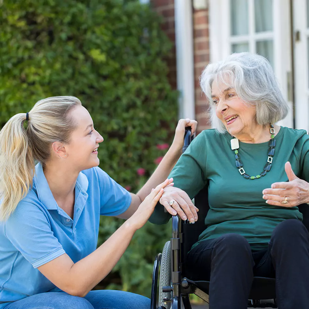 Old woman sitting on a wheel chair while talking to her support worker in the garden