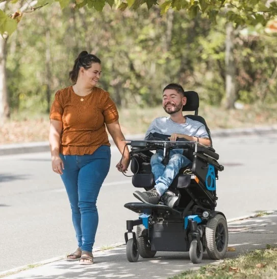 Happy disabled man in a wheel chair on a stroll outside with his support worker